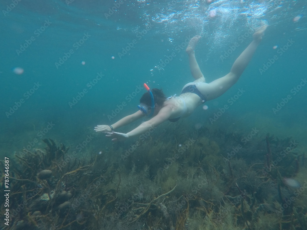 A woman snorkels and swims underwater on a coral reef in the ocean