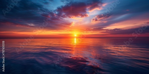 A beautiful sunset over the ocean with a large sun in the sky. The sky is filled with clouds and the water is calm