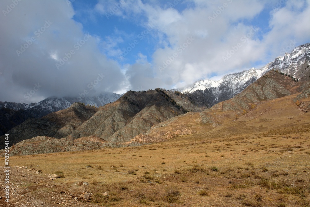 The edge of the dried autumn steppe at the foot of a high mountain range under a cloudy autumn sky. The edge of the dried autumn steppe at the foot of a high mountain range under a cloudy autumn sky.