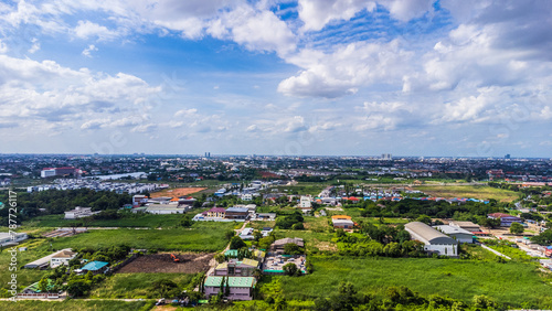 Aerial view of the rice fields and the winding roads between the rice fields. There is a group of tall buildings. The sky was clear blue with fluffy white clouds.