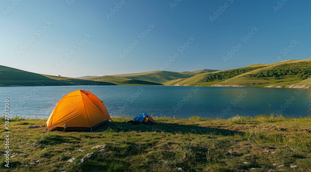 Discover tranquility at a serene lake as an orange tent stands on its shore amidst green hills, basking in the golden hour glow under a clear blue sky. AI generative.