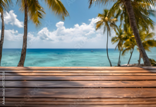 Tropical beach view with wooden deck foreground and palm trees against a clear blue ocean and sky.