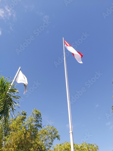 the red and white flag under a cloudy blue sky in the afternoon. The Indonesian flag flying in the sky, Indonesia is almost damaged by age which has been partially torn, fluttered high in the hills.
