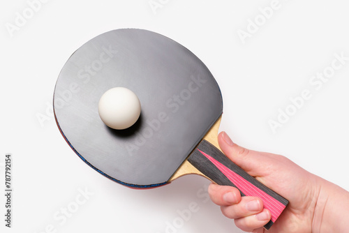 Female hand holding a racket with ping pong ball on a white background, top view.