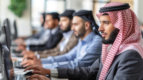  A man in a headscarf uses a laptop in front of him Other men sit at desks, each focused on their own screens