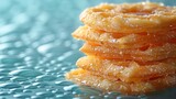   A stack of orange donuts rests atop a blue glass table, dotted with water droplets on its surface