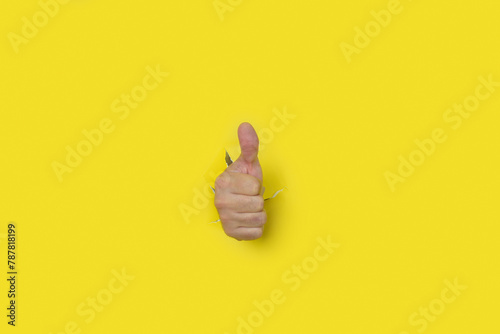 Hand with thumb up as a sign of approval, coming out of the hole of a yellow torn paper background. photo