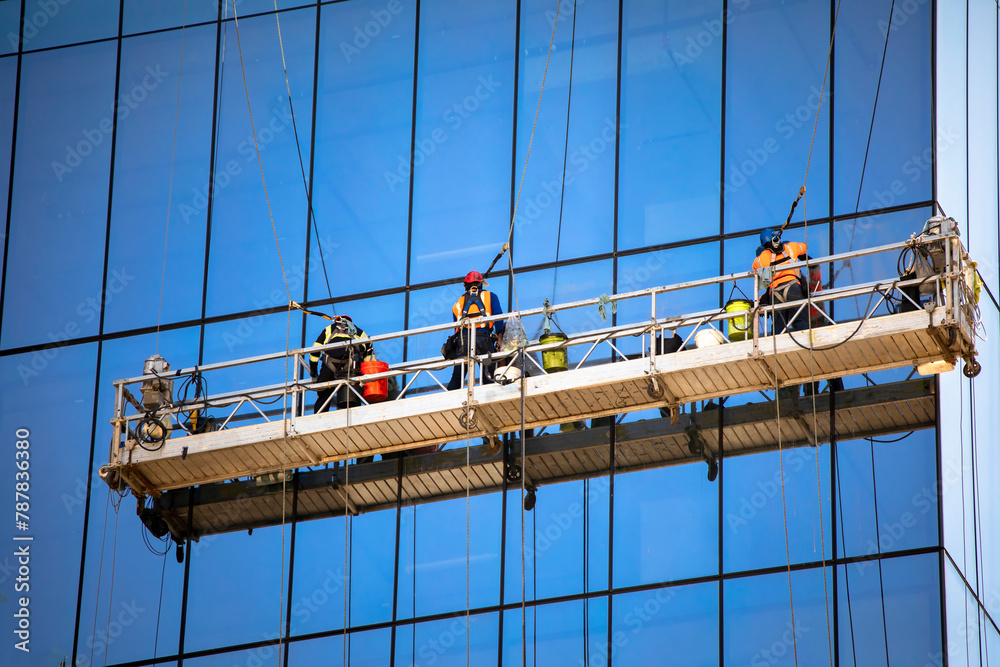 Side view shot of three window washers on a hanging scaffold on a commercial building with blue glass