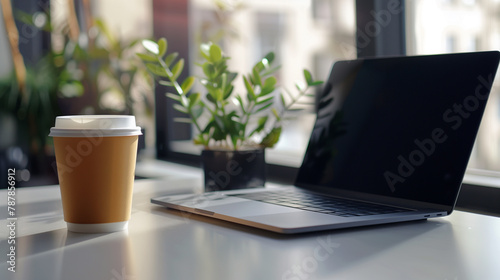 Laptop with recyclable coffee cup on table in modern office, coffee break for relaxation at work