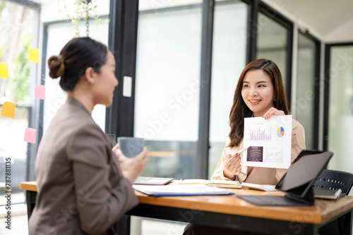 Engaged businesswoman presenting a colorful financial report during a collaborative meeting with a coworker in an office.
