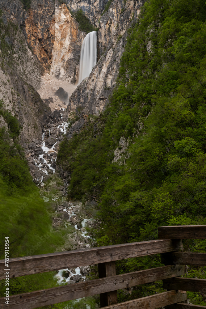 Boka waterfall in Slovenia, near Bovec. Easy trekking nature trail in the forest with the view of the immense waterfall overhanging the mountains visible from the road, long exposure photography. Boka waterfall in Slovenia, near Bovec. Easy trekking nature trail in the forest with the view of the immense waterfall overhanging the mountains visible from the road, long exposure photography.