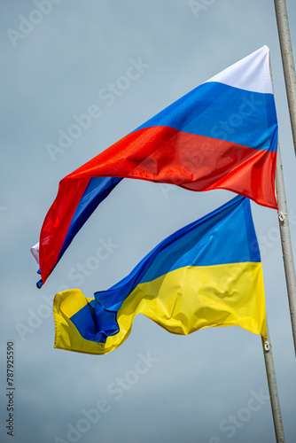 Russian and Ukrainian flags are waving with wind over blue sky. Low angle view. Dispute and conflict concept. Horizontal composition with copy space.