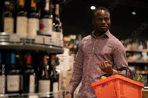 Tablou pe pânză African American Man in a supermarket choosing a wine