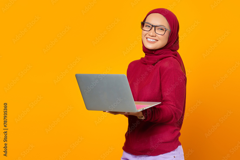 Portrait of smiling asian woman holding laptop over yellow backg Portrait of smiling asian woman holding laptop over yellow backg