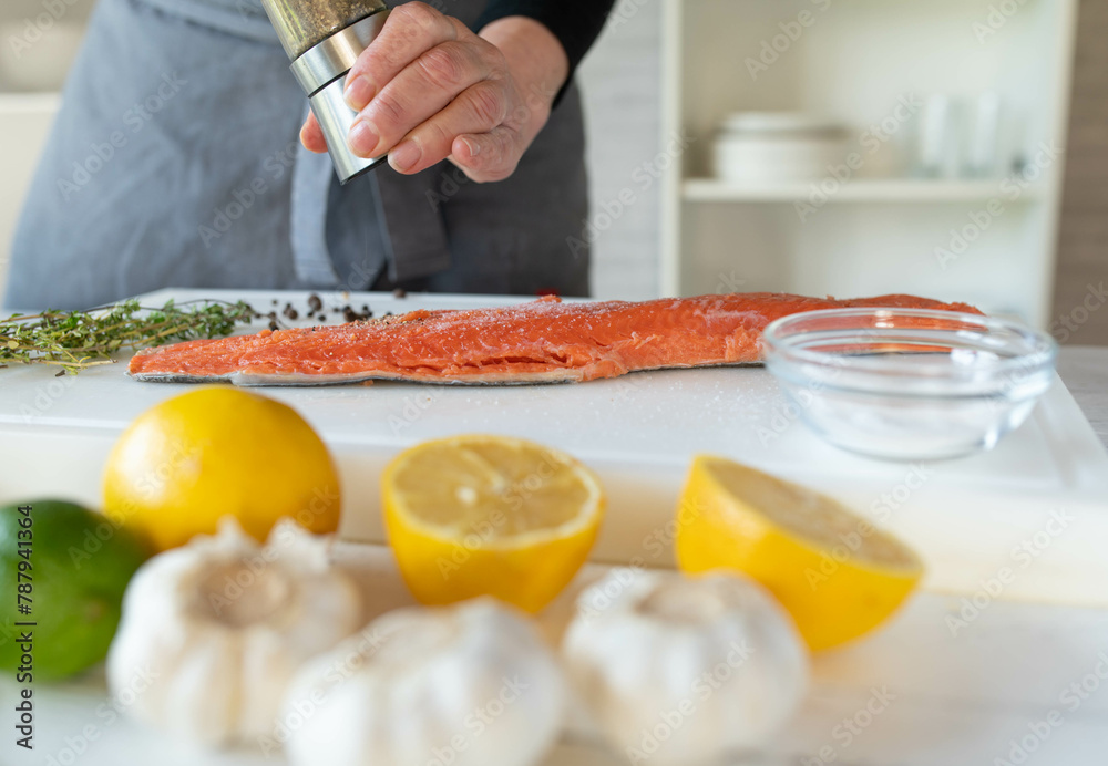Person seasoning a raw half salmon fillet with a pepper shaker on a cutting board