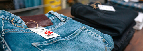 Close up of label with discount price over a blue jeans pants on vintage store. Sales season and black friday concept. Banner of apparel stacks ready to sell on clothes shop with industrial style.