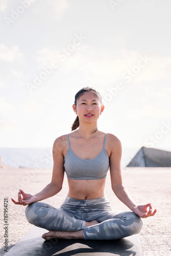 young asian woman doing meditation by the sea sitting on a yoga mat, concept of mental relaxation and healthy lifestyle, copy space for text