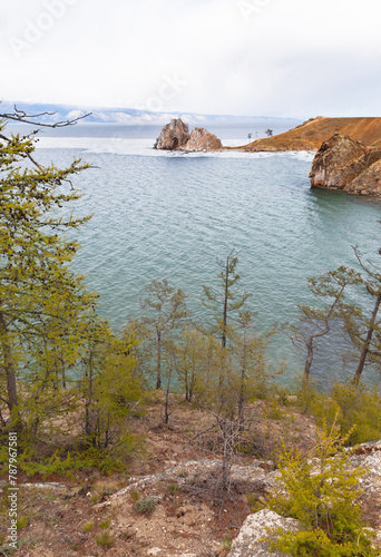 Baikal Lake in May. View of the shore of Olkhon Island with green larches, the famous Shamanka Rock - natural landmark of the lake, and ice drift in the Small Sea. Spring landscape. Natural background