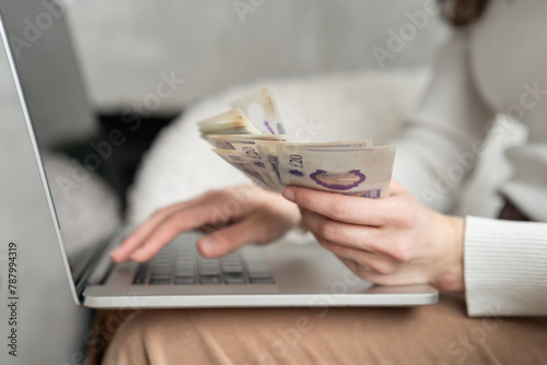 Close-up of a woman holding a handful of cash while using a computer photo