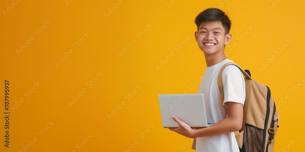 A delighted young male student stands holding a laptop with a backpack, with a vibrant yellow background emphasizing positivity A delighted young male student stands holding a laptop with a backpack, with a vibrant yellow background emphasizing positivity