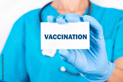 A doctor in blue medical uniform holds a card with the name of the diagnosis, the word Vaccination. Medical concept.