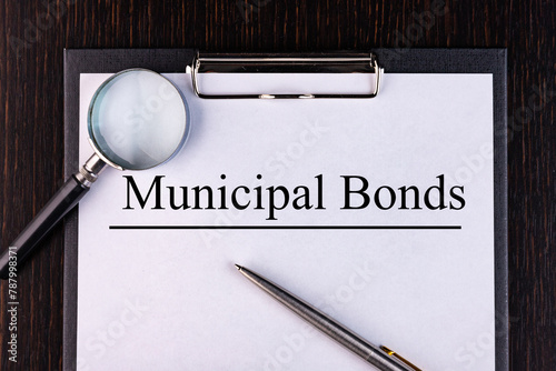 Text MUNICIPAL BONDS is written on a notebook with a pen and a magnifying glass lying on the table. Business concept. photo