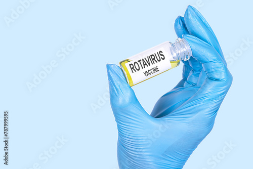 ROTAVIRUS VACCINE text is written on a vial whose ampoule is held by a hand in a medical disposable glove. Medical concept.