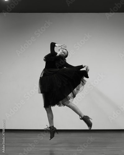 Ballerina on a white background, she is in a black dress. A brunette girl poses in front of the camera. Beautiful dancer, black and white style.