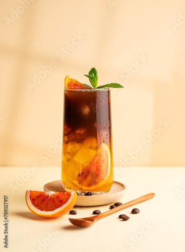 Americano coffee with orange juice (bumble) in a tall glass with ice and mint on a yellow background