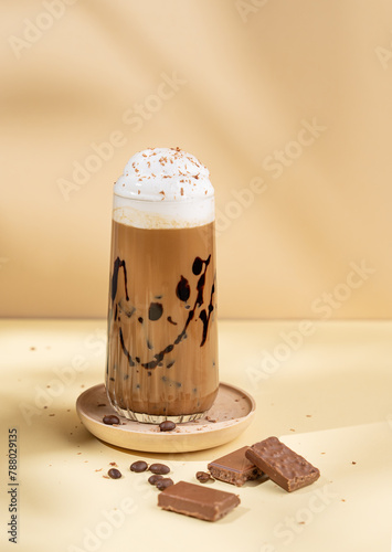 Cold chocolate coffee drink or milkshake with whipped cream in a tall glass on a yellow background