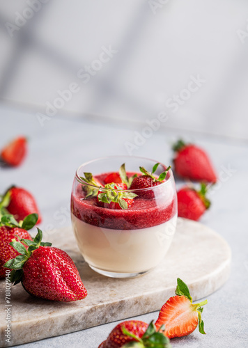 Strawberry and cream panna cotta in glass with fresh berries on a marble board on a light background with shadow.