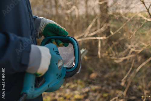 Close-up of a man trimming branches in a garden with an electric hedge trimmer