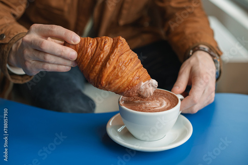 Close-up of a man sitting in a cafe dipping a croissant in a cup of coffee photo
