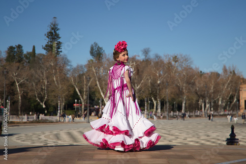 Girl dancing flamenco, posing on her back looking over her shoulder, in typical flamenco costume on a bridge in a beautiful square in Seville. Dance concept, flamenco, typical Spanish, Seville, Spain.