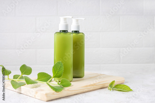 cosmetic bottles on a wooden board and a sprig of mint on a gray background