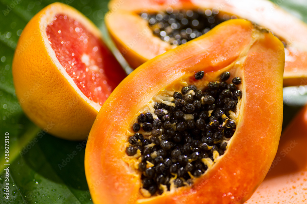 Exotic fruits background. Papaya and orange citrus fresh fruits on tropical leaf green background with shadows of palm tree. Halved fresh organic Papayas and grapefruit exotic fruits close up Exotic fruits background. Papaya and orange citrus fresh fruits on tropical leaf green background with shadows of palm tree. Halved fresh organic Papayas and grapefruit exotic fruits close up