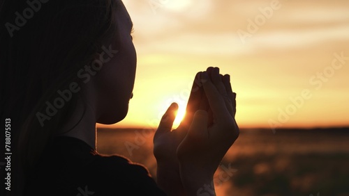Woman praying with folded hands at sunset silhouette. Religious pious orthodox christian spiritual believing faithful girl at morning dawn sunrise reading prayer bible turning to god jesus christ.