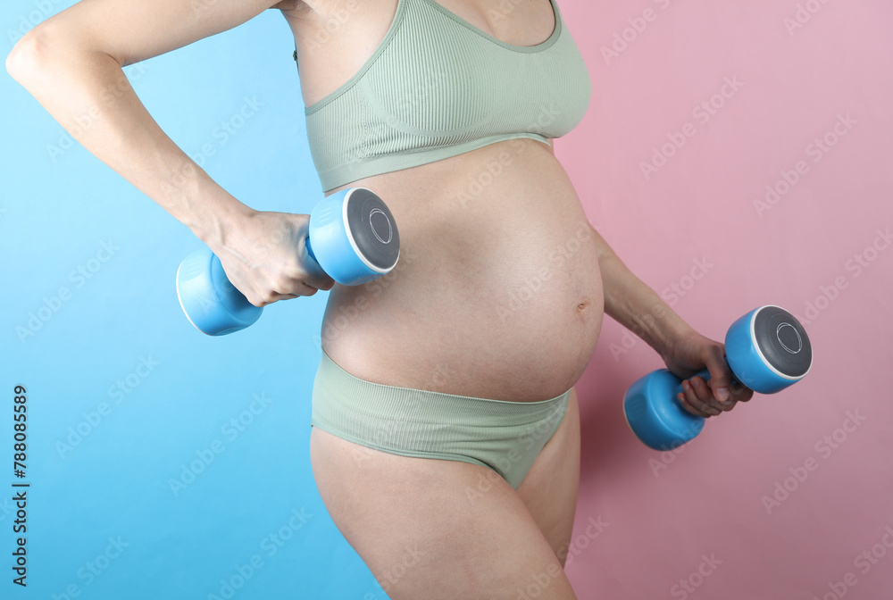 Pregnant woman in underwear holding dumbbells on blue pink background. Exercising during pregnancy Pregnant woman in underwear holding dumbbells on blue pink background. Exercising during pregnancy