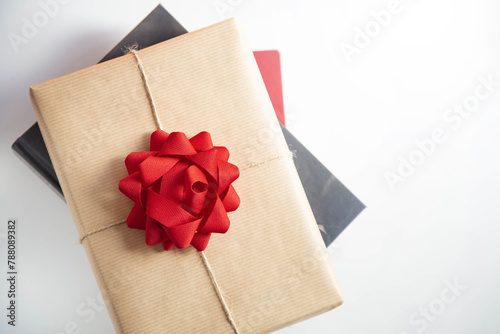 Tope view of the book wrapped in a gift paper with a red bow is on the other books on the table. Book Day, International Book Giving Day. 