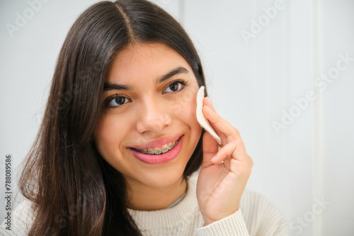 Female Latin teenager with braces using make up cotton pad. © Ladanifer