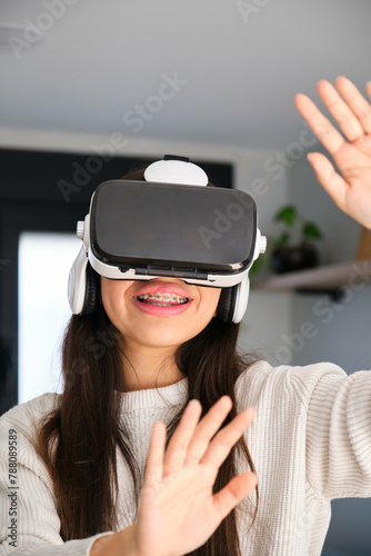 Female Latin teenager with braces using virtual reality glasses at home.
