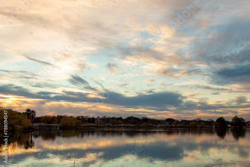 Dramatic sunset clouds reflection along the treelined horizon  on Woodlawn Lake San Antonio Texas