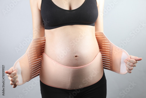 Young Pregnant woman with orthopedic belt for back and belly support. Bandage for pregnant women. Special belt for the 3rd trimester. Studio shot on a gray background