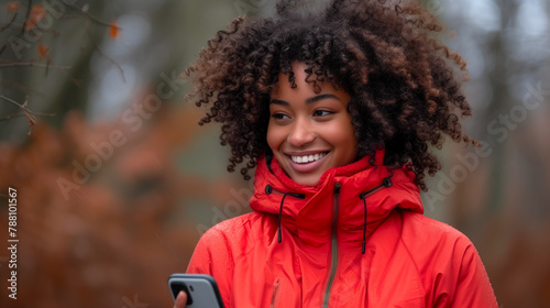 Joyful young woman with a radiant smile using her phone in a park during autumn.