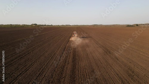 Aerial rear view of tractor harrowing a field at sunset.