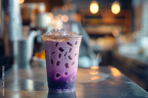 Iced purple drink taro iced milk tea in a clear cup on a bar, with a blurred background photo