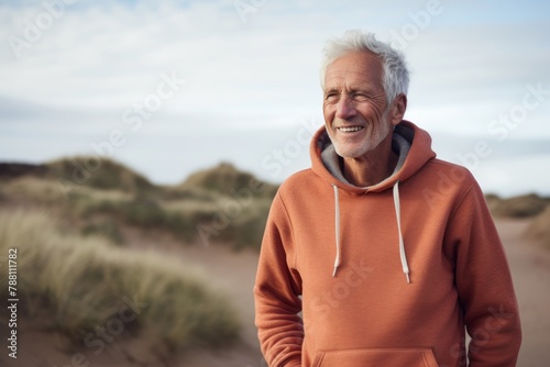 Portrait of a happy man in his 70s dressed in a comfy fleece pullover while standing against serene dune landscape background