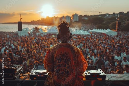 A DJ oversees a throng of party-goers at a beachside event, as the sunset casts a warm glow over the scene