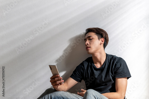 asian man heartache looking at phone alone. sad depressed moody people regret emotional background. despair indoors home asian male person sitting suffering from grief frustration pain with sick face