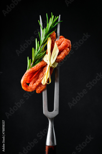 Dried pork sausages on a metal fork. Kabanos Close up on a black background. © Yaruniv-Studio